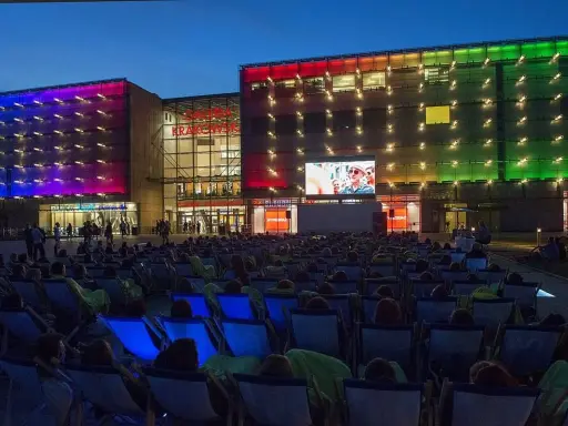 Wieczorny seans pod gołym niebem przed Galerią Krakowską. Tłum widzów w leżakach ogląda film na wielkim ekranie.