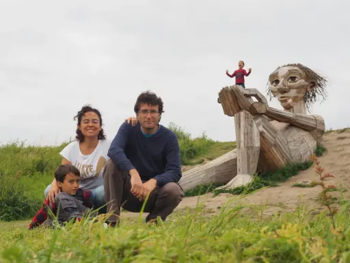 Familia disfrutando de Copenhague con niños, posando ante una escultura gigante de madera. Un niño pequeño juega en la mano de la figura.