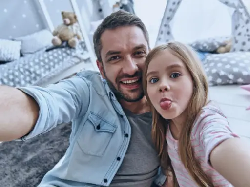Padre e figlia si scattano un selfie giocoso, un'immagine che cattura la gioia del loro rapporto padre-figlia, quasi come in un'interpretazione freudiana della felicità.