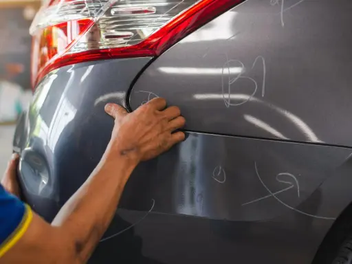 Ręce mechanika oceniają wgniecenia na karoserii samochodu, przygotowując się do usuwania uszkodzeń.