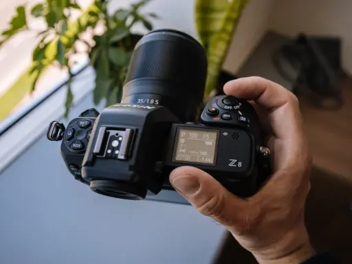Dłoń trzyma aparat Nikon Z8 z obiektywem 35/1.8 S. Ekran pokazuje ustawienia, a cena tego modelu jest atrakcyjna.