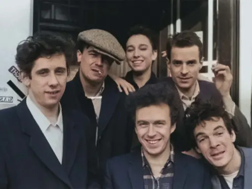 Medlemmar av the Pogues poserar glatt utomhus, några med cigaretter.