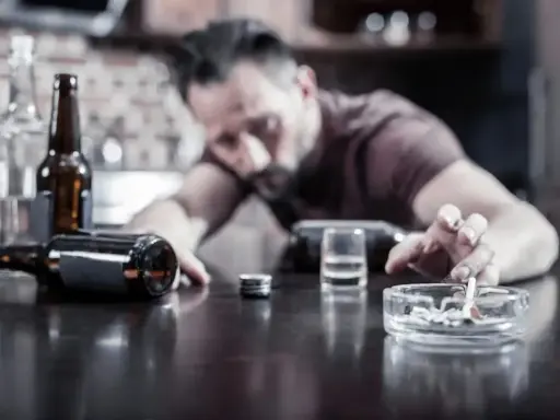 Mężczyzna z papierosem w popielniczce, obok butelki i kieliszka. Czy to skutek uboczny po doxycyclinum i alkoholu?