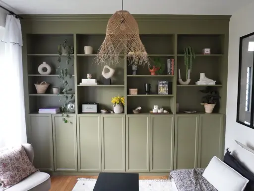 Une belle idée de bibliothèque salon avec des étagères vertes remplies de vases, plantes, livres et objets déco.