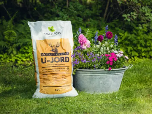 En säck Hasselfors U-jord bredvid en zinkbalja fylld med färgglada blommor i kruka.