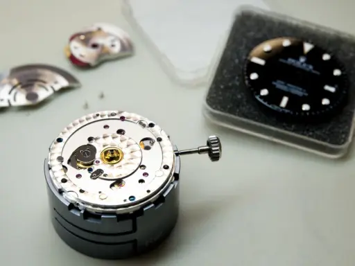 Parti di un movimento di orologio di lusso, tra cui il quadrante nero e la corona, pronti per l'assemblaggio.