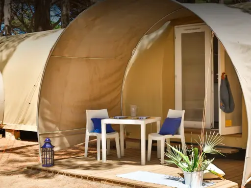 Tavolino e sedie con cuscini blu davanti a una tenda del **Gitavillage Il Gabbiano**. Lanterna blu e piante sul deck.