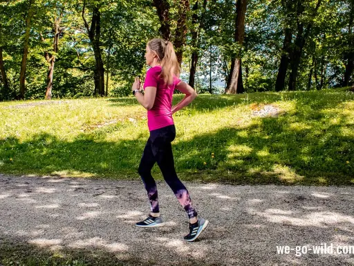 Frau läuft im Wald, um sich aufzuwärmen. Sonnenschein und grüne Bäume schaffen eine idyllische Kulisse für ihr Training.