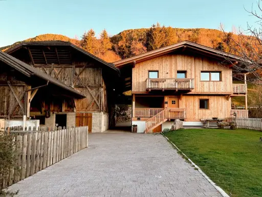 Maso Gallo Rosso: un'accogliente casa in legno e un fienile rustico immersi nel paesaggio alpino al tramonto.