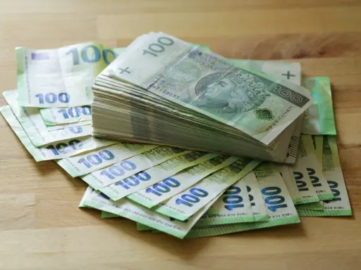 Stos banknotów 100 zł i 100 euro na drewnianym blacie. Może to być kwota na zasiłek stały.