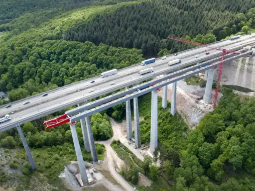 Wysoki wiadukt z betonowymi filarami, na którym widać ruch samochodowy. Konstrukcja z betonu C30/37 wznosi się nad zielonym lasem.