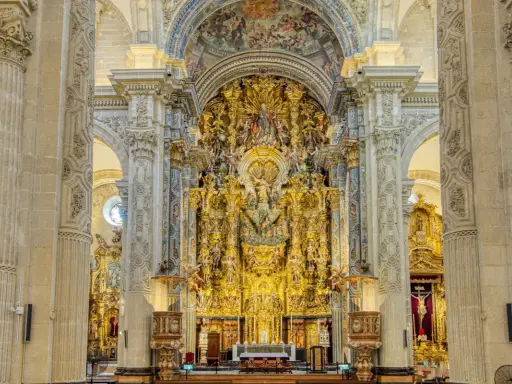 Prunkvoller Altar im Kathedrale Sevilla Innenraum, verziert mit goldenen Skulpturen und Malereien, die eine himmlische Szene darstellen.
