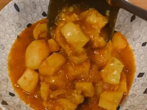 Un plato de papas con choco en una salsa naranja, servido en un cuenco con un patrón de puntos.