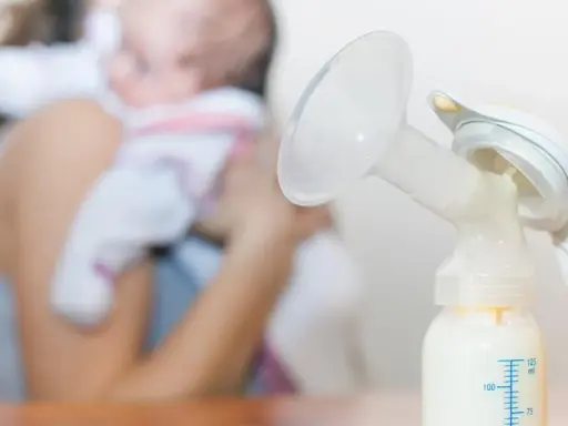 Laktator z butelką mleka, w tle mama z dzieckiem. Zastanawiasz się, ile trwa nawał mleczny?