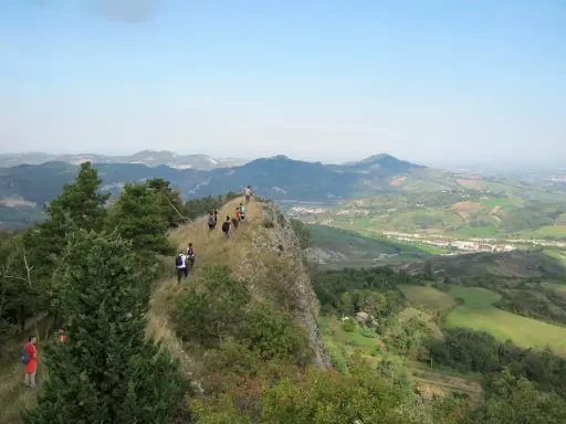 Un gruppo di escursionisti fa trekking su un crinale roccioso con vista panoramica sulle colline verdi, un'avventura indimenticabile vicino a Rimini.