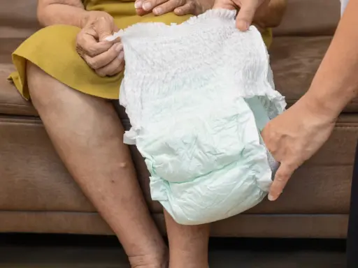 Mani che mostrano come si mette il pannolino a un'anziana seduta.