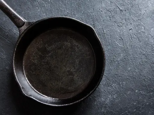 Eine schwarze Stahlpfanne, bereit für das Einbrennen, liegt auf einer dunklen, texturierten Oberfläche.