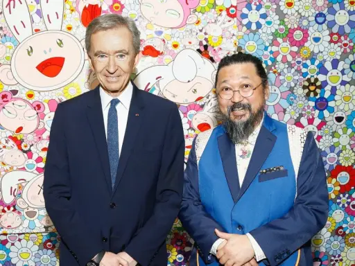 Two billionaire art collectors, Bernard Arnault and Takashi Murakami, pose in front of Murakami's signature smiling flower art.