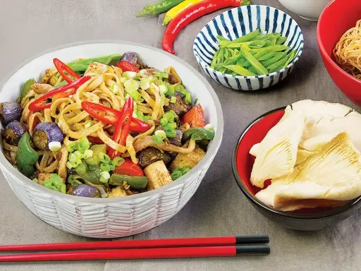 Pikantny makaron z tofu, bakłażanem, papryką i szczypiorkiem. Obok miseczki z fasolką szparagową i grzybami.