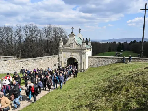Pielgrzymka wchodzi przez zabytkową bramę. W oddali widać krzyż i piękne krajobrazy, które są nowa słupia atrakcje.