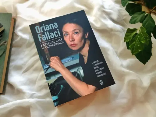 Książka "Kapelusz cały w czereśniach" Oriany Fallaci leży obok okularów i innych książek.