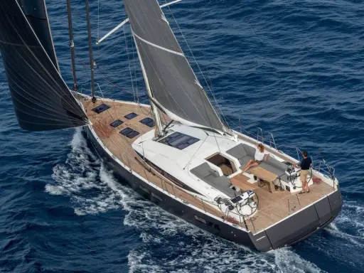 Un couple profite d'une croisière sur un voilier habitable à l'année, naviguant sur des eaux bleues par une journée ensoleillée.