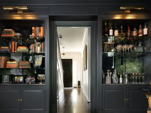 Estanterías oscuras con libros, botellas y copas. Ideas para como decorar una libreria con estilo y elegancia.