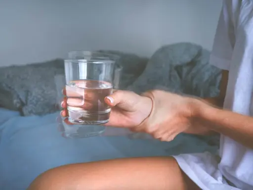 Drżąca ręka trzyma szklankę wody. Objawy mogą wskazywać na atak padaczki alkoholowej. Co robić?