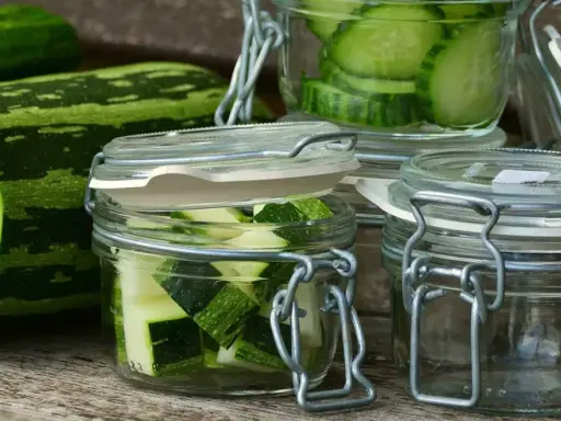 Zucchini-Scheiben und -Würfel in Gläsern, bereit zum einkochen im Dampfgarer. Frische Zucchini liegt daneben.