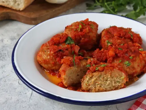 Polpette di pane succulente in salsa di pomodoro, guarnite con prezzemolo fresco. Un piatto casalingo che profuma di tradizione.