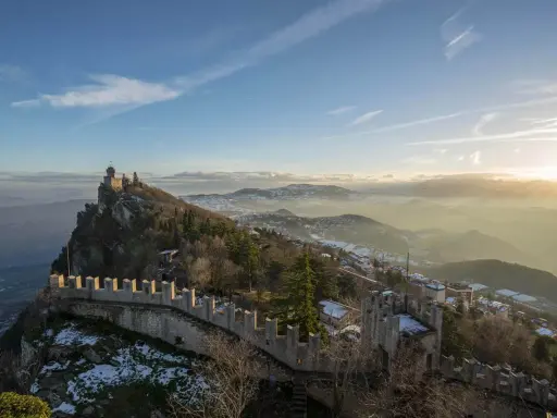 Un suggestivo viaggio a San Marino: torri medievali su un crinale roccioso, con la nebbia che avvolge le valli sottostanti al tramonto.