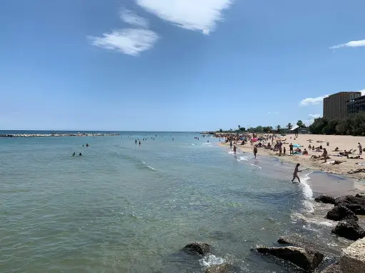 Sonniger bari strand mit vielen Menschen, die im Meer schwimmen und sich am Sand sonnen.