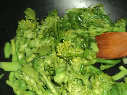 Cime di rapa salteados en sartén con una cuchara de madera. Verduras verdes vibrantes y frescas, listas para ser disfrutadas.