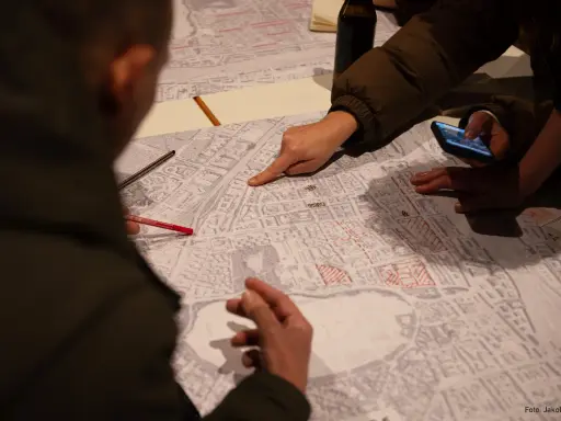 Menschen diskutieren auf einer Karte, die Details der Stadt zeigt. Sie planen die monitoring soziale stadtentwicklung, markieren Bereiche und nutzen ein Smartphone.