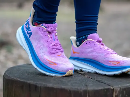 Fioletowe buty Hoka Clifton na pniu drzewa. Hoka to firma znana z amortyzacji.