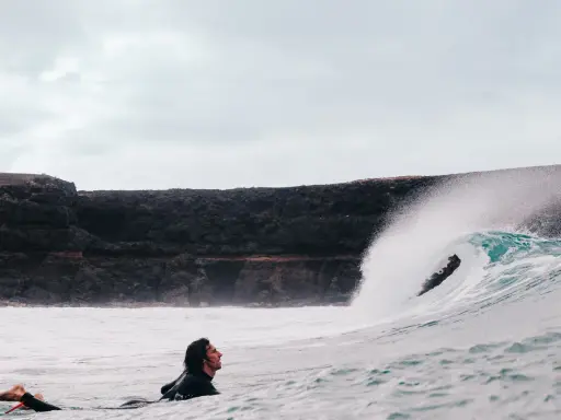 Surfer wartet auf die perfekte Welle vor einer Felswand, um Costa Calma surfen zu gehen.