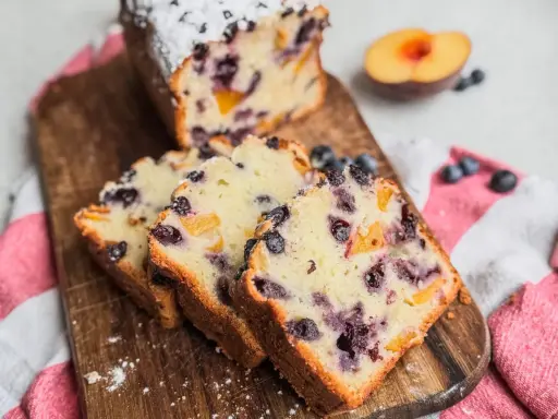 Saftiger Joghurt Kuchen mit Blaubeeren und Pfirsichstücken, bestäubt mit Puderzucker.