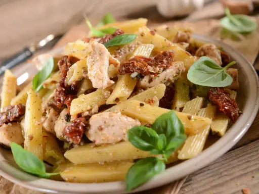 Penne z kurczakiem i suszonymi pomidorami, ozdobione świeżą bazylią. Pyszne danie, które zachwyci każdego smakosza.