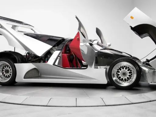 Silberner Lotec C1000 Supersportwagen mit geöffneten Türen und Hauben, rote Sitze und sichtbarer Motor.