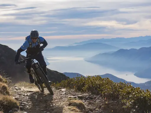 Ein Mountainbiker auf einer abenteuerlichen Tour in den Alpen, mit einem See und Bergketten im Hintergrund.