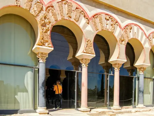 Verzierte Bögen und Säulen der Medina Azahara spiegeln sich in Glas. Besucher bestaunen die historische Architektur.
