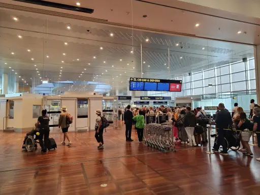 Ludzie w terminalu lotniska, tablice z informacjami o bramkach i pasażerowie z bagażami.