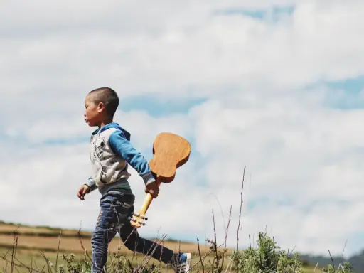 Kleines Kind, 17 Monate, sehr anstrengend, rennt mit Ukulele über Feld.