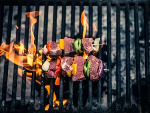 Brochetas de carne y verduras sobre parrilla de carbón, llamas naranjas. ¡Así se hace barbacoa carbón!