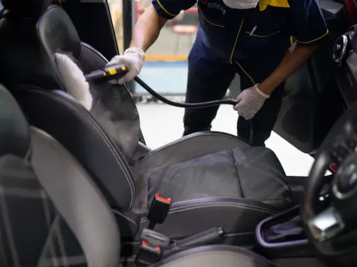 Un profesional usa vapor para limpiar los asientos del coche, mostrando cómo limpiar los asientos del coche de forma efectiva.