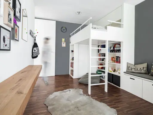 Ein weißes Hochbett mit integrierten Regalen und Stauraum bietet viele Ideen unterm Hochbett für Spielzeug und Bücher. Ein Holzbalken und ein Kuhfell-Teppich ergänzen den Raum.