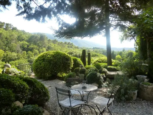 Le jardin de la louve, un havre de paix verdoyant avec une table et des chaises invitant à la détente, surplombe une vallée luxuriante.