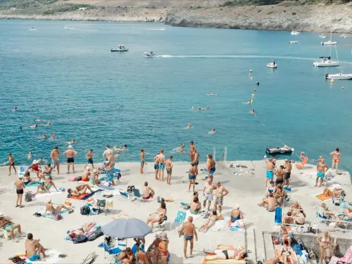 Gente in spiaggia e in mare a Santa Maria di Leuca, con barche all'orizzonte.