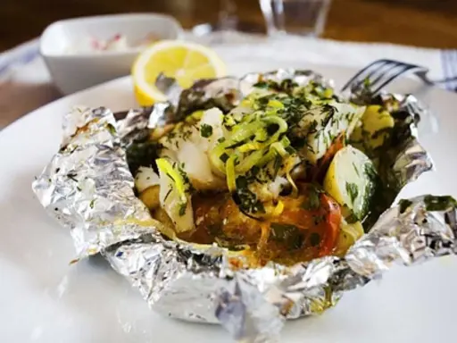 En läcker fiskpaket i ugn med potatis, tomat och örter, toppad med citron och purjolök. Enkel och smakrik middag.