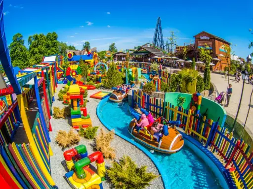 Parque acuático colorido con atracciones para niños en Cracovia. Barcas navegan por un río azul rodeado de juegos y vallas vibrantes.